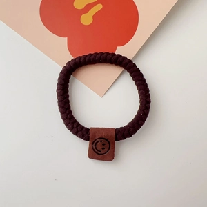 Close-up of brown elastic braided hair tie with a smiley face leather patch detail