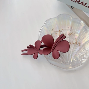 Vue détaillée de la pince à cheveux double papillon bordeaux mat sur un plateau coquillage