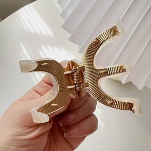 Detailed view of golden alloy hair claw clip with cream acetate inlay and radial textures