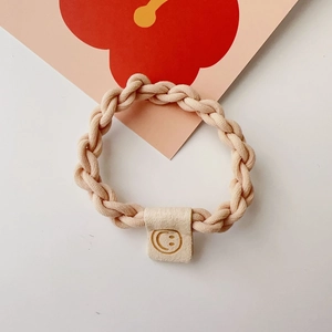 Close-up of a beige elastic braided hair tie featuring a cute smile face fabric label