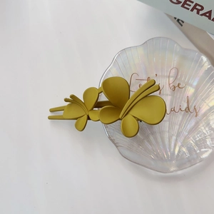 Détail d'une pince à cheveux papillon jaune moutarde mate sur un plateau décoratif