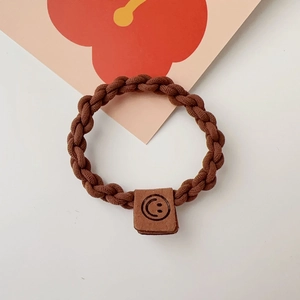 Detail of a brown braided elastic hair tie featuring a square leather patch with a smiley face