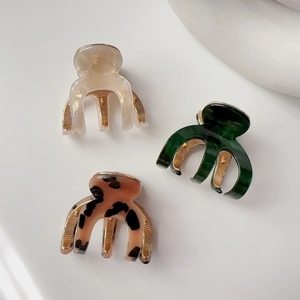Three acetate mini hair claws in cream, dark green, and tortoiseshell with gold springs
