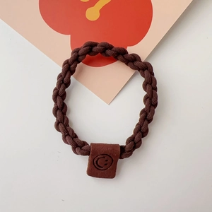 Close-up of brown braided elastic hair tie with a small leather square smiley face detail