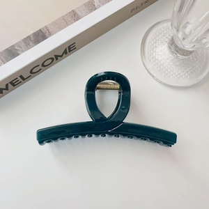 Dettaglio molletta per capelli verde scuro con manico circolare su sfondo bianco