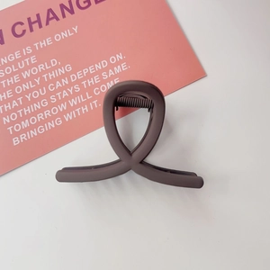 Détail de la pince à cheveux mate marron foncé avec design à boucles entrelacées sur fond blanc