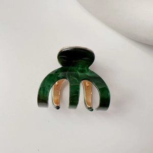 Macro shot of dark green marble acetate hair claw with elegant golden metal teeth detail