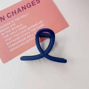 Détail d'une pince à cheveux bleue foncée mate avec un design croisé sur un bureau