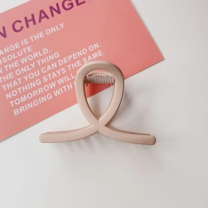 Pince à cheveux rose nude mat avec design croisé géométrique sur fond esthétique doux