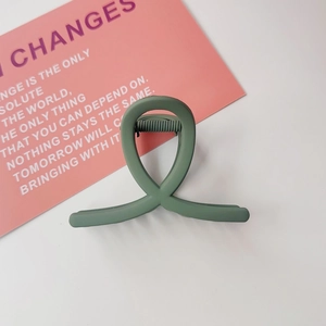 Détail d'une pince à cheveux torsadée vert Morandi mat sur une surface blanche