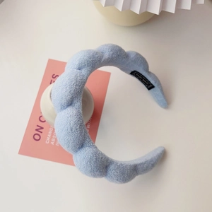 Close-up of light blue braided sponge headband with black woven handmade label on white desk