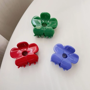 Close-up of three acetate flower hair claws in red, green and purple on a white stand