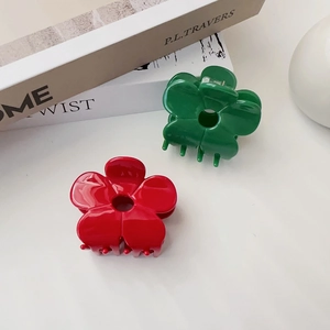 Close-up of red and green acetate flower hair claws showing glossy finish and five-petal design