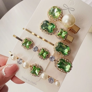 Close-up of 5 vintage hair clips with emerald rhinestones and white pearls on card