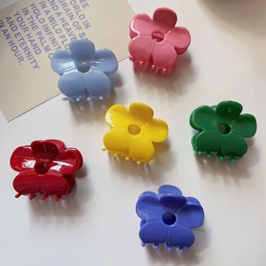 Flat lay of six colorful flower claw clips in pink, blue, and yellow on a cream surface