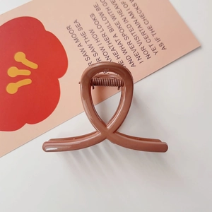 Détail d'une pince à cheveux mate marron caramel avec design torsadé et ressort métallique
