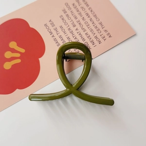 Détail d'une pince à cheveux croisée vert olive sur un fond esthétique épuré