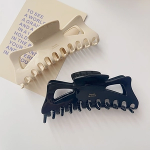 Détail des grandes pinces à cheveux crème et noire avec inscription dorée élégante