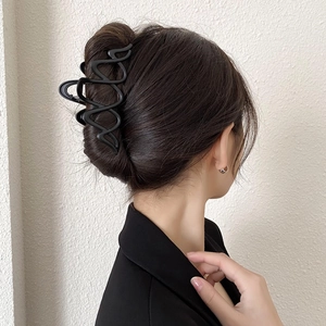 Detail view of a large black wavy shark clip securing a French twist hairstyle on a model