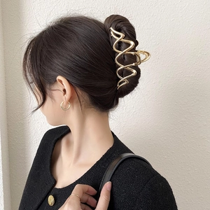 Elegant gold metal shark hair claw with irregular wave design worn on a female model