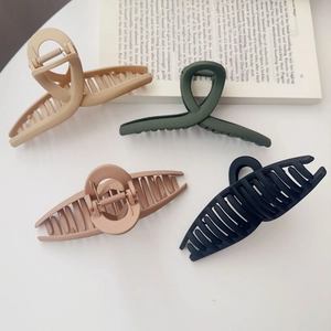 Gros plan de quatre pinces à cheveux mates en beige, vert, rose et noir sur blanc