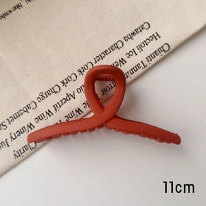 Détail d'une pince à cheveux orange mate de 11 cm sur un fond blanc minimaliste