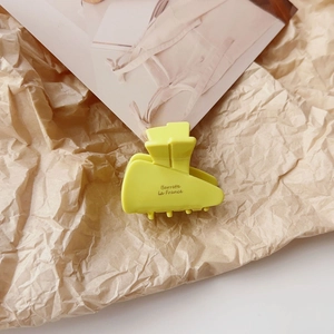 Detail view of a bright yellow matte hair claw clip on textured paper with fashion card