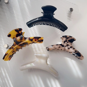 Detail of four acetate hair claws in black, tortoiseshell, and cream on a tray