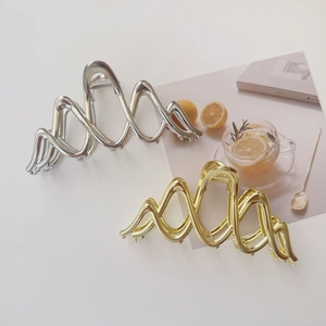 Detailed view of large gold and silver wavy metal hair claws on a white surface