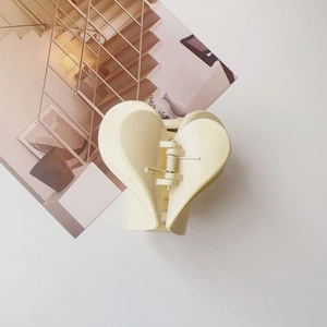 Dettaglio molletta per capelli a cuore color panna lucida su sfondo minimalista