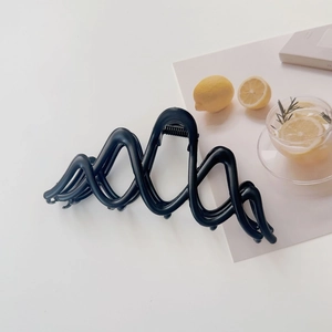 Detail shot of a matte black wavy hair claw clip showing a strong metal spring and teeth