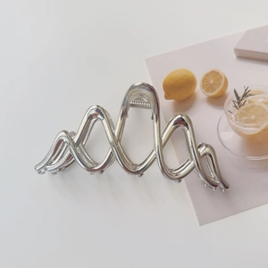 Close-up of a large silver metal hair claw clip with a sleek wavy mountain geometric design