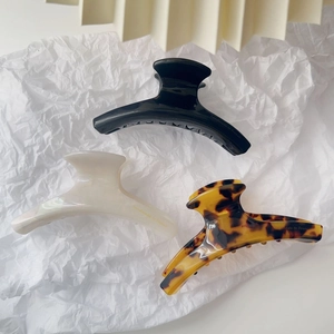 Three acetate hair claws in black, cream white and leopard print colors on textured paper