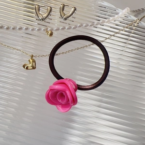 Vue détaillée d'un chouchou rose en forme de rose et colliers coeur doré sur plateau