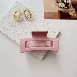 Close-up of matte pink speckled hair claw and gold resin earrings on a white stone base