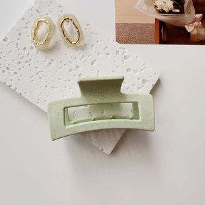 Close-up of mint green speckled hair claw clip and beige oval earrings on white block