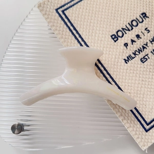 Detail of cream acetate hair claw with gold handmade lettering on glass tray
