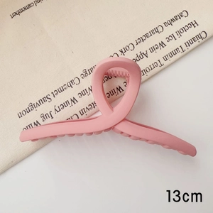 Détail d'une pince à cheveux rose mat de 13cm avec design torsadé sur tissu épuré