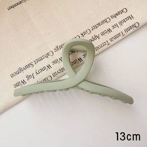Gros plan d'une pince à cheveux mate vert sauge de 13 cm avec un design croisé élégant