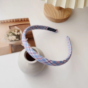 Detailed close-up of blue plaid headband with handmade label on white ceramic vase