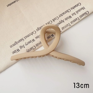 Détail d'une pince à cheveux beige mat de 13 cm avec un design géométrique torsadé