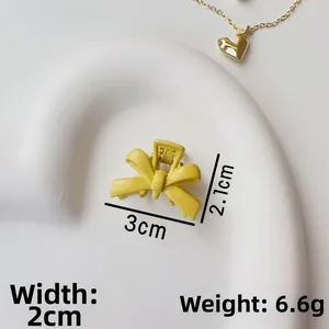 Detail view of a matte yellow metal bow hair claw clip showing 3cm length on white tray