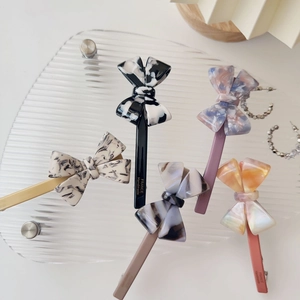 Detail of five handmade acetate bow hair clips with elegant marble patterns and gold text