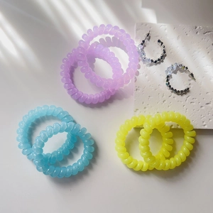 Macro detail of colorful spiral hair ties and silver rhinestone hoop earrings on stone
