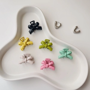 Set of six matte colorful bow-shaped metal hair claws in a white ceramic tray