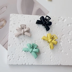 Detail of four matte pastel bow-shaped hair clips on a textured stone surface