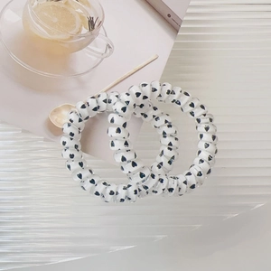 Close-up of two spiral hair ties with black heart patterns on white wavy display board