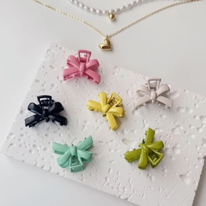 Set of six colorful matte bow hair clips arranged on a white textured stone surface