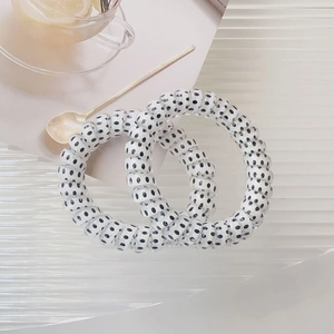 Detail view of two white spiral telephone wire hair ties with black polka dots on a tray