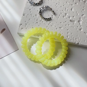 Neon yellow spiral hair ties and silver earrings on a white stone surface with elegant light